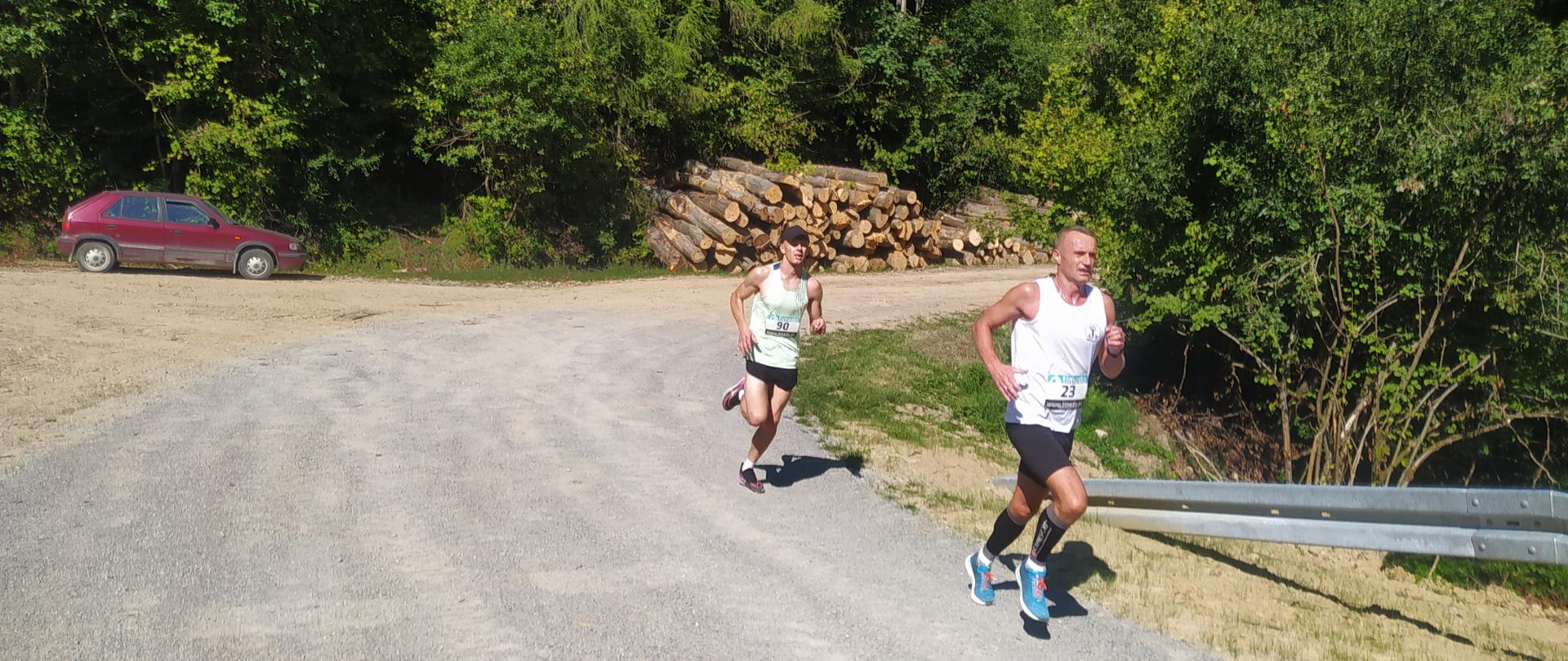 dwóch biegnących sportowców po gruntowej drodze w terenie leśnym