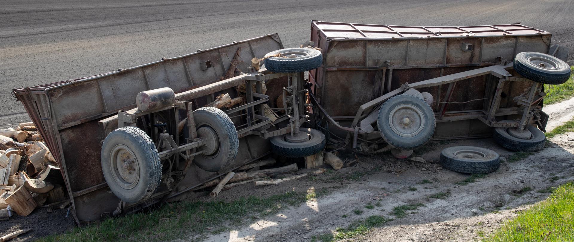 Two tractor trailers full of tree logs rolled over in field from dirt road