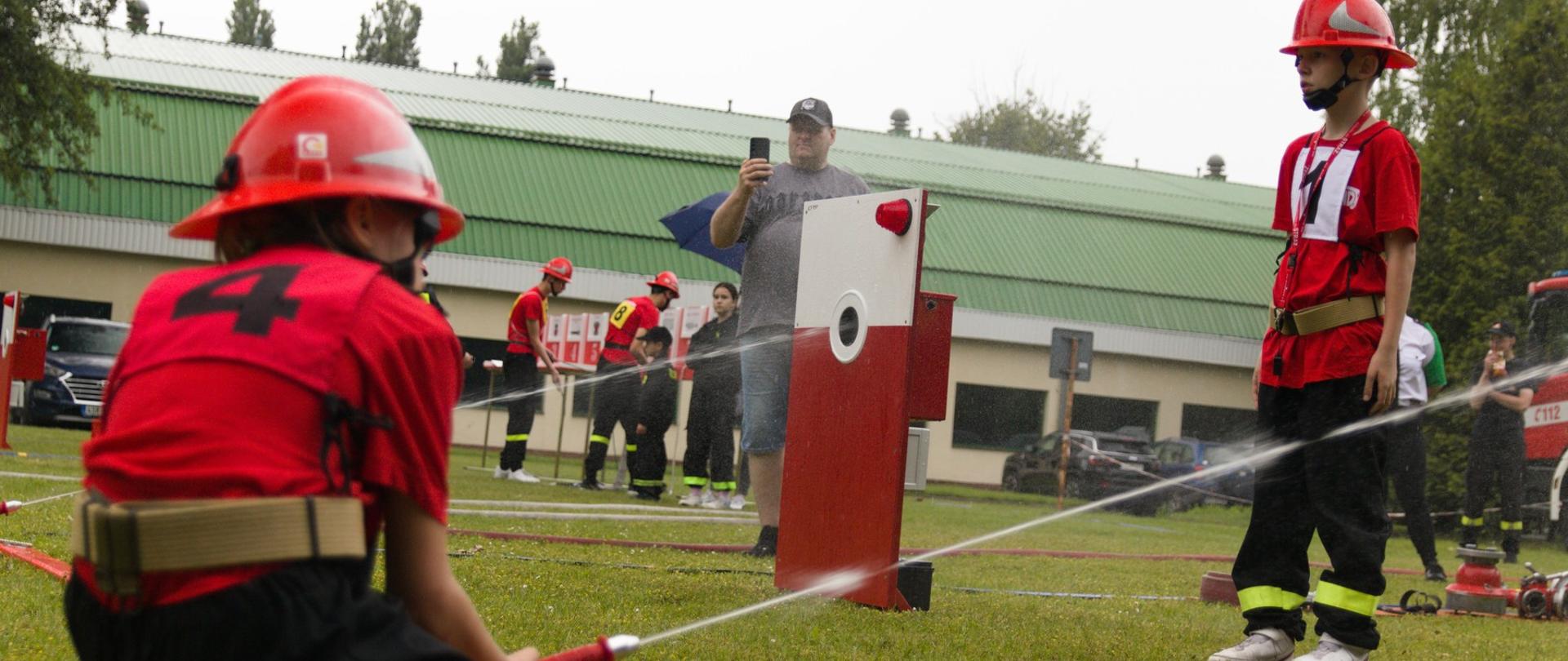 Zdjęcie wykonane podczas XIII Powiatowych Zawodów Młodzieżowych Drużyn Pożarniczych powiatu pabianickiego. Na zdjęciu zawodnicy jednej z Młodzieżowych Drużyn Pożarniczych podczas konkurencji ćwiczenia bojowego.