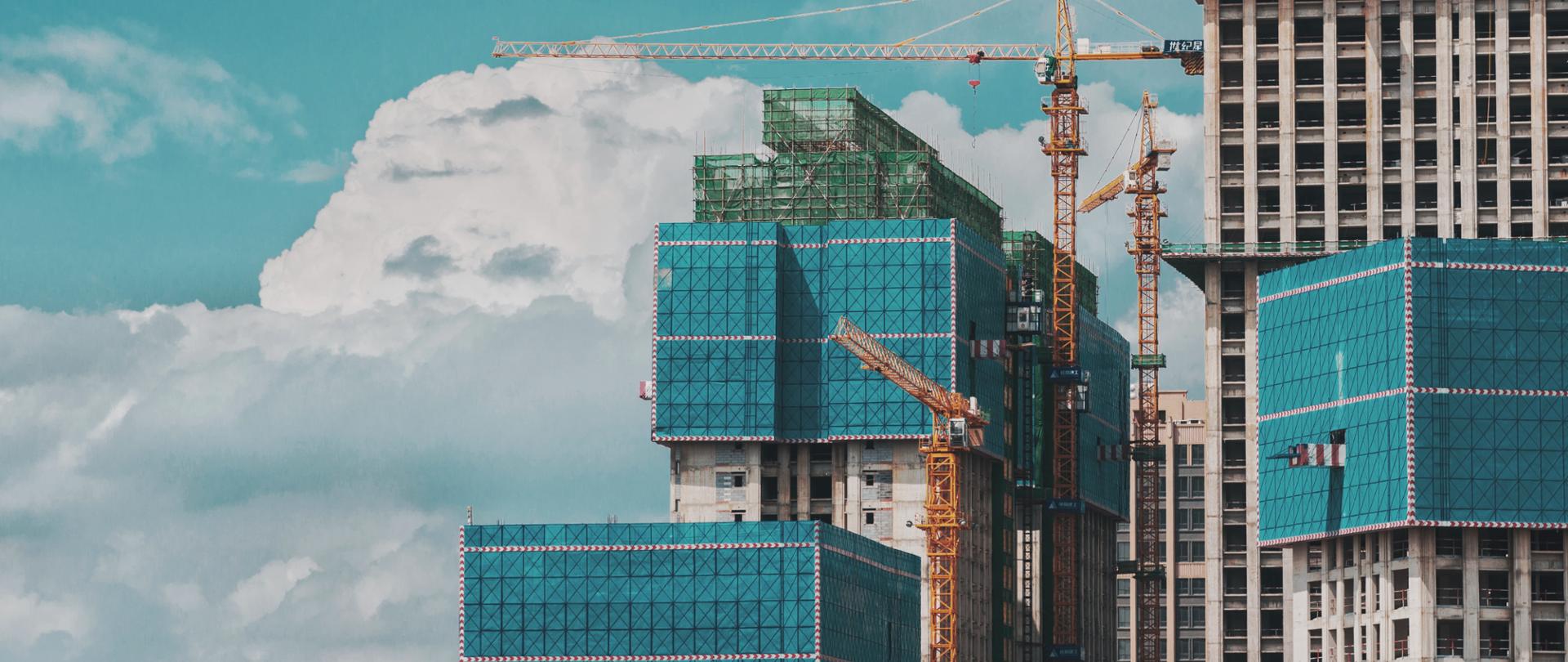zdjęcie przedstawia osiedle w budowie, obok budowli stoją dźwigi