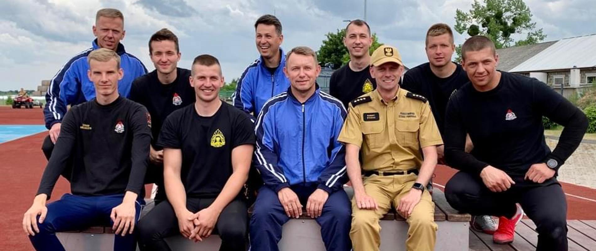 Reprezentacja KP z Komendantem Powiatowym PSP w Wąbrzeźnie. Zawodnicy oraz Komendant siedzą na stopniach podium. 