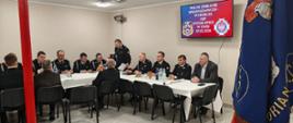 Na zdjęciu widoczny jest Komendant Powiatowy PSP w Ostrowcu Św., wójt gminy Wąśniów oraz druhowie OSP podczas zebrania sprawozdawczo-wyborczego. Uczestnicy siedzą przy stole, jeden z druhów stoi i jest w trakcie odczytywania działalności OSP w 2025 r.