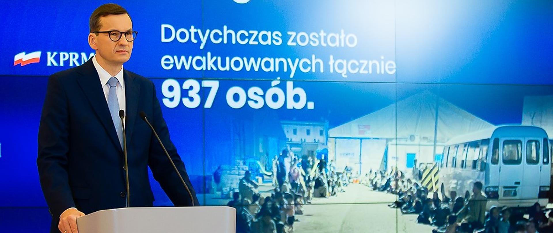 Premier Mateusz Morawiecki przy mównicy. W tle ścianka multimedialna z prezentacją.