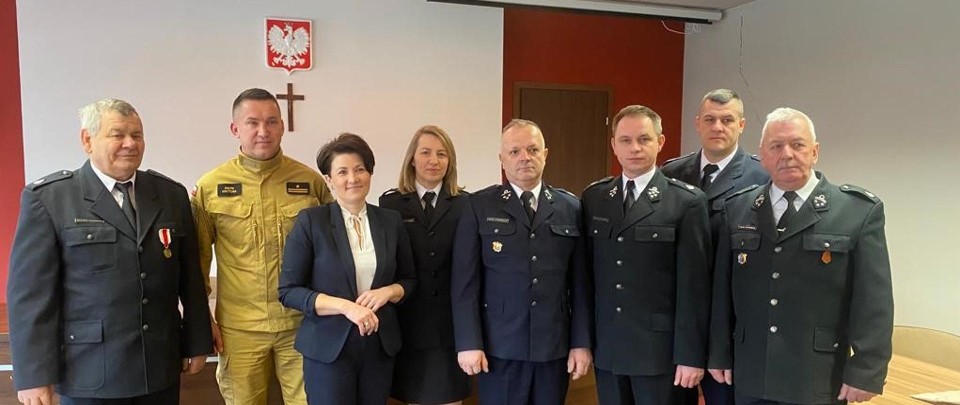 stojące osoby które wcześniej podpisywały porozumienie oraz reprezentację druhów OSP Gnieszowice pozują do zdjęcia Strażacy OSP wśród których jest jedna druhna ubrani są w czarne mundury wyjściowe.