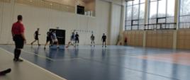 Hala sportowa. Zawodnicy w strojach granatowych oraz bordowych grają w piłkę nożną