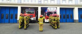 Strażacy stojąc na baczność na tle samochodów gaśniczych oddają cześć poległym strażakom z Ukrainy.