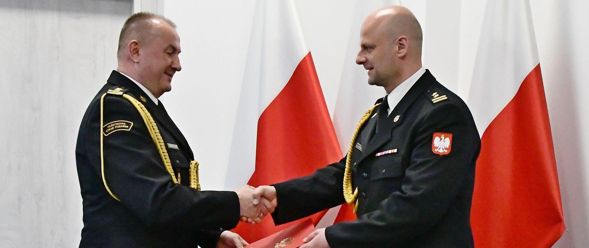 Pomorski Komendant Wojewódzki Państwowej Straży Pożarnej starszy brygadier Jacek Niewęgłowski składa gratulacje oraz wręcza decyzję o powołaniu na stanowisko Komendanta Powiatowego Państwowej Straży Pożarnej w Lęborku brygadierowi Leszkowi Formela. W tle widoczne trzy flagi państwowe.