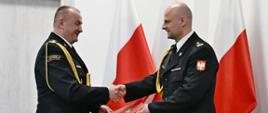 Pomorski Komendant Wojewódzki Państwowej Straży Pożarnej starszy brygadier Jacek Niewęgłowski składa gratulacje oraz wręcza decyzję o powołaniu na stanowisko Komendanta Powiatowego Państwowej Straży Pożarnej w Lęborku brygadierowi Leszkowi Formela. W tle widoczne trzy flagi państwowe.