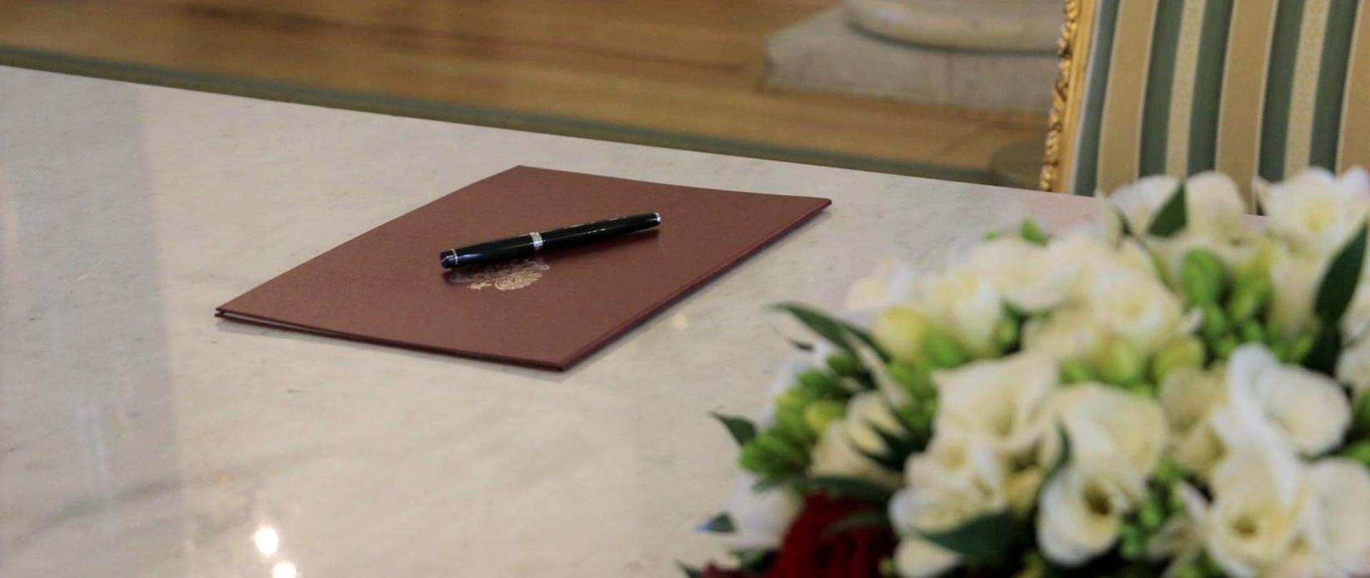 Na zdjęciu znajduje się akt ratyfikacyjny Porozumienia AGN w czerwonej oprawie, który leży na blacie. 