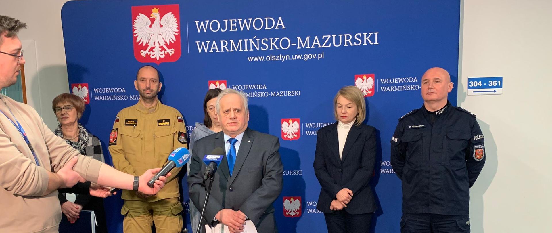 Wicewojewoda przed mikrofonem na konferencji prasowej, odpowiada na pytania dziennikarzy