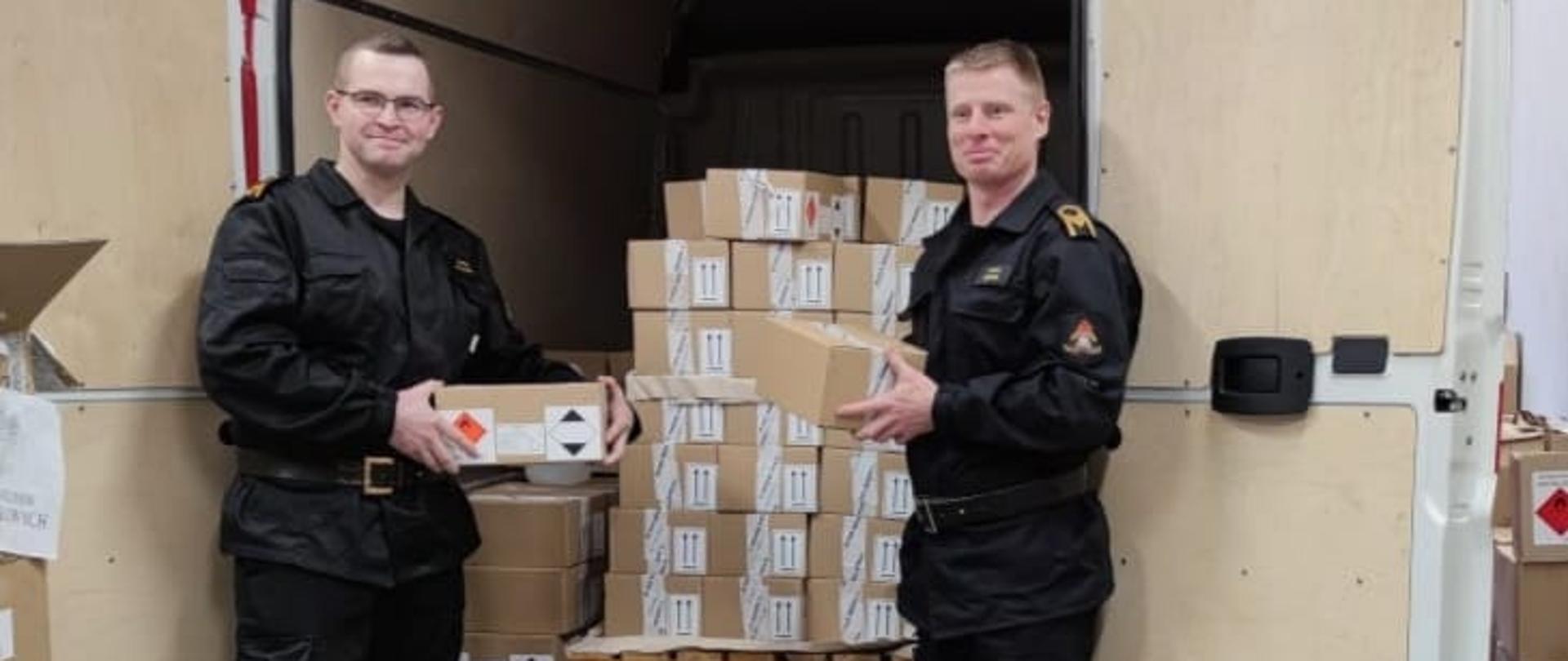 Dwaj strażacy z paczkami stoją przed samochodem