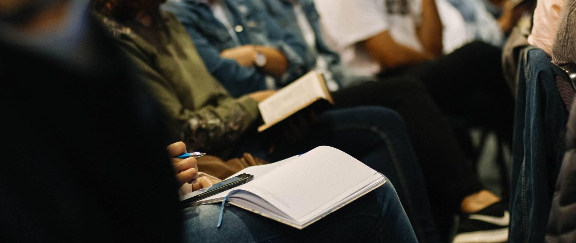 osoby siedzące w rzędzie trzymające notatniki na kolanach