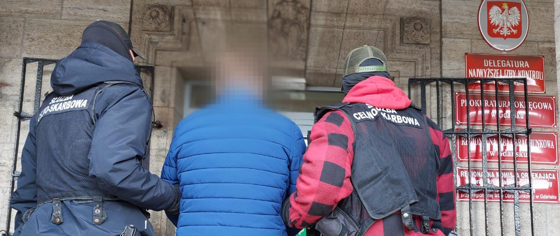 Funkcjonariusze Służby Celno-Skarbowej prowadzą zatrzymaną osobę.