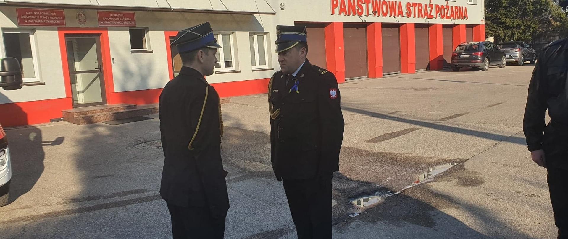 Funkcjonariusz stoi na wprost komendanta, który wręczył mu akt mianowania, podczas uroczystej zmiany służby na placu komendy.