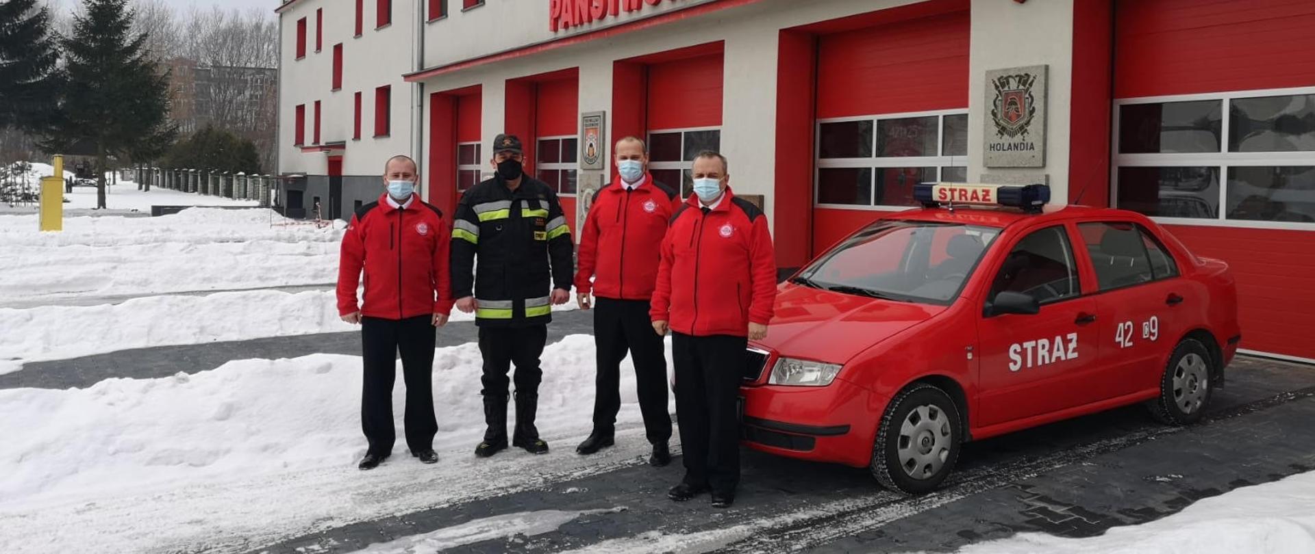 Zdjęcie przedstawia samochód Skoda Fabia na tle frontu budynku Komendy Powiatowej PSP w Chełmnie. Przy samochodzie stoi trzech druhów z OSP Kijewo Królewskie ubranych w czerwone polary oraz Komendant st.bryg. Karol Utrata w mundurze dowódczo-sztabowym i kurtce. 