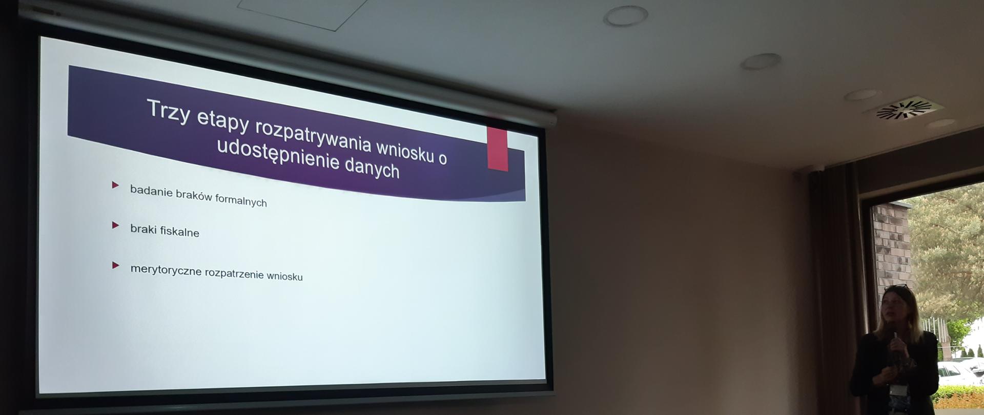 prelegentka z mikrofonem patrzy na ekran z prezentacją