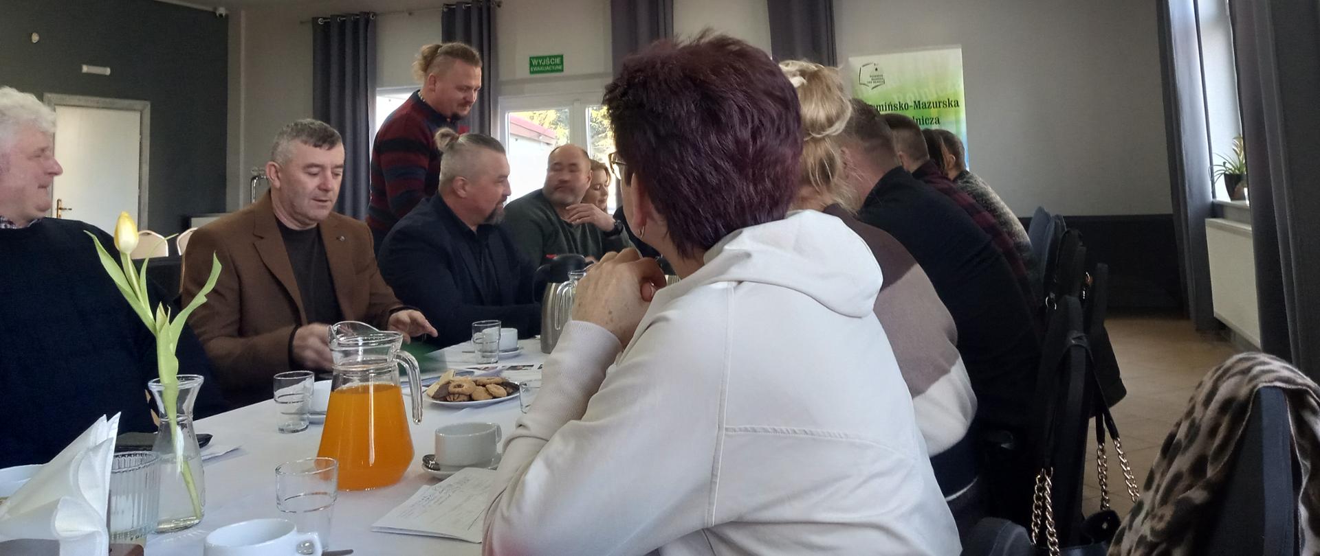 grupa siedzi przy długim stole po obu jego stronach w tle baner WMIR