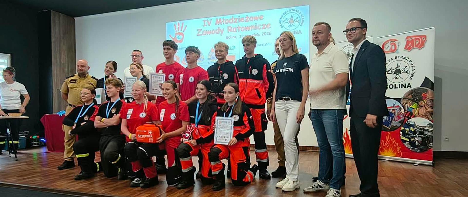 Zdjęcie przedstawia uczestników IV Młodzieżowych Zawodów Ratowniczych. Na zdjęciu podium zawodów z organizatorami przedsięwzięcia. 