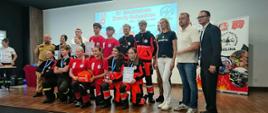 Zdjęcie przedstawia uczestników IV Młodzieżowych Zawodów Ratowniczych. Na zdjęciu podium zawodów z organizatorami przedsięwzięcia. 