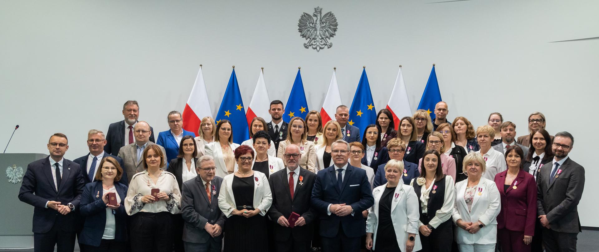 Zdjęcie grupowe po uroczystości. W tle widoczne są oficjalne flagi: biało-czerwona oraz unijna.