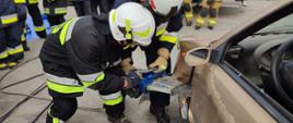 Druhowie OSP ubrani w ubrania specjalne, hełmy ćwiczący użycie rozpieracza hydraulicznego.