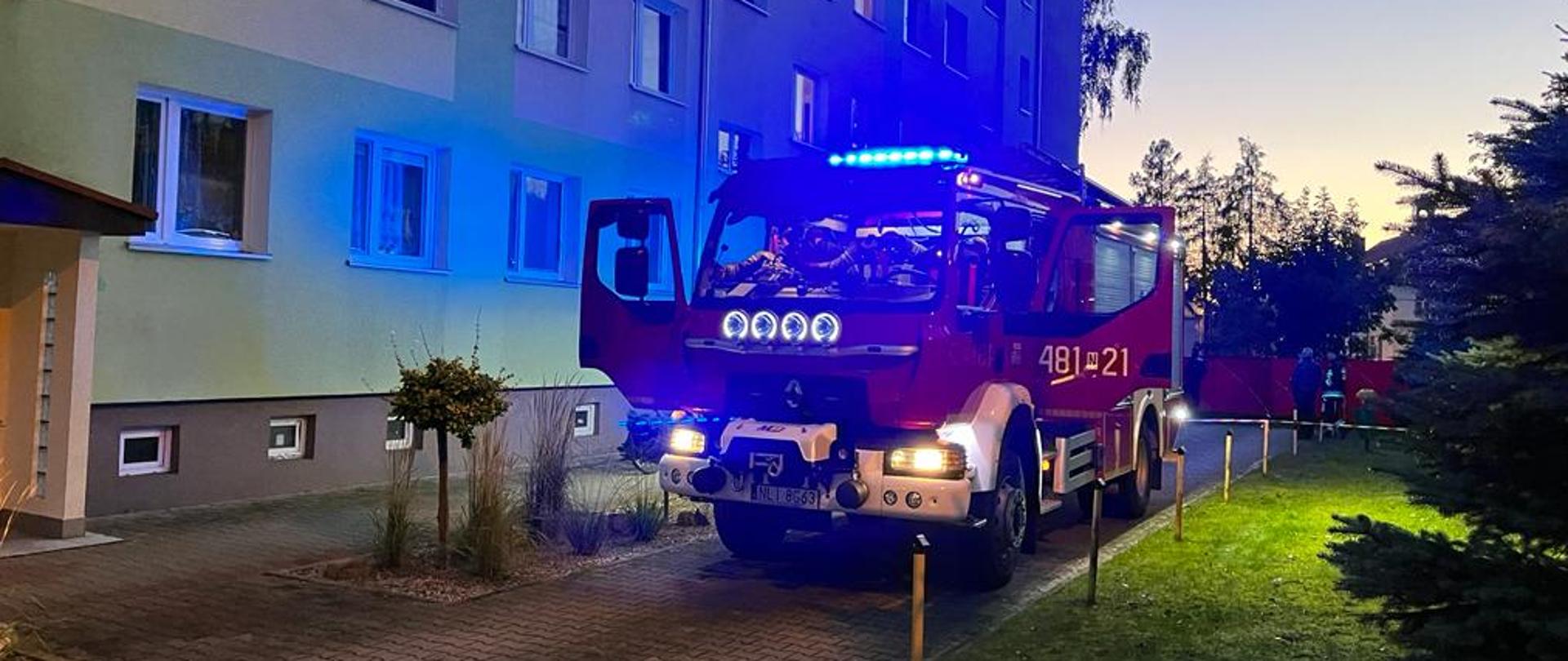 Zdjęcie przedstawia pojazd pożarniczy na tle budynku gdzie miał miejsce pożar