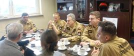 Widok ogólny. 5 funkcjonariuszy Państwowej Staży Pożarnej i 3 osoby siedzące przy stole omawiają wykonanie dokumentacji projektowej.