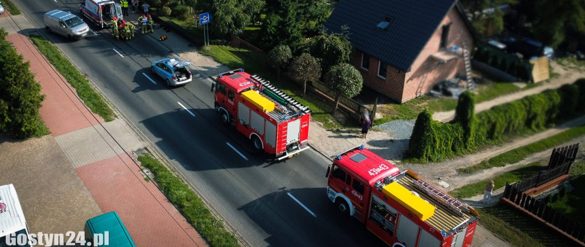 Zdjęcie z lotu ptaka, które przedstawia dwa samochody pożarnicze, patrol Policji, karetkę pogotowia oraz strażaków.