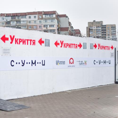 Biała ścian z logo Polskiej pomocy, Lublina, miasta Sumy i czerwonymi napisami w języku ukraińskim Do ukrycia 