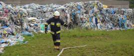 Akcja na składowisku odpadów. Na tle pryzmy odpadów strażak trzymający w ręce prądownicę. Obok niego leży rozwinięty wąż. 