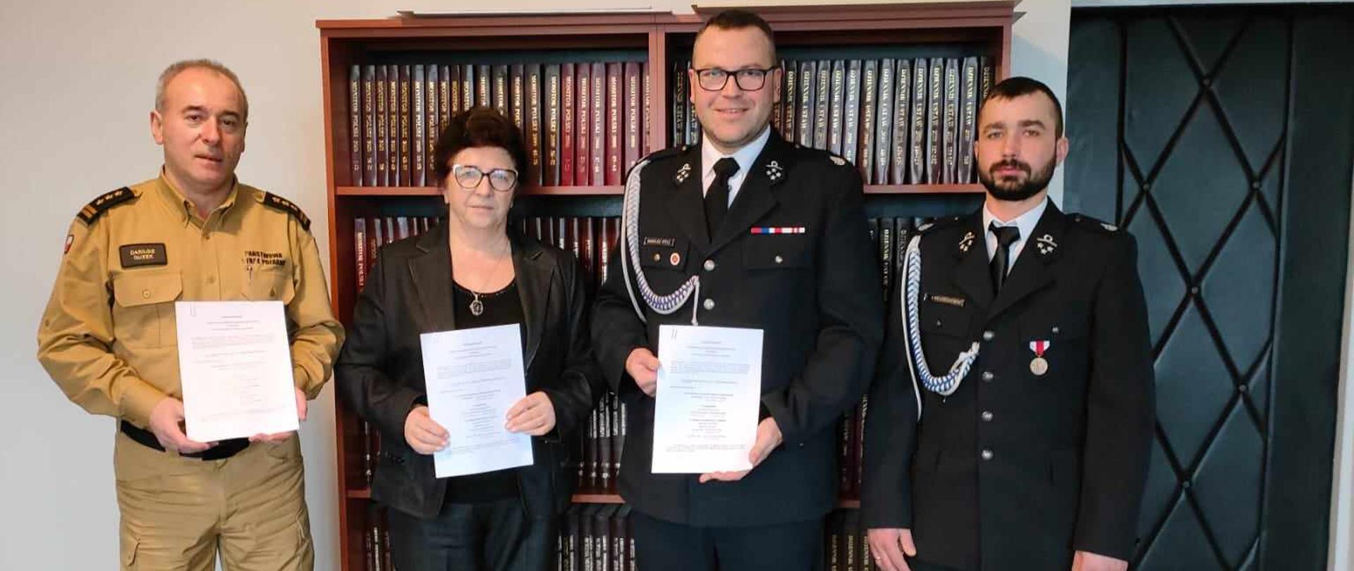 Biuro w budynku gminy dmosin cztery osoby prezentują podpisane dokumenty w sprawie włączenia OSP Lubowidza do krajowego systemu ratowniczo gaśniczego są to wójt gminy dmosin pani Danuta Supera, komendant powiatowy psp w brzezinach starszy brygadier Dariuszz Guzek, Prezes Ochotniczej Straży Pożarnej w Lubowidzy druh Mariusz Rydz,
Naczelnik Ochotniczej Straży Pożarnej w Lubowidzy druh Eryk Wojciechowski
.