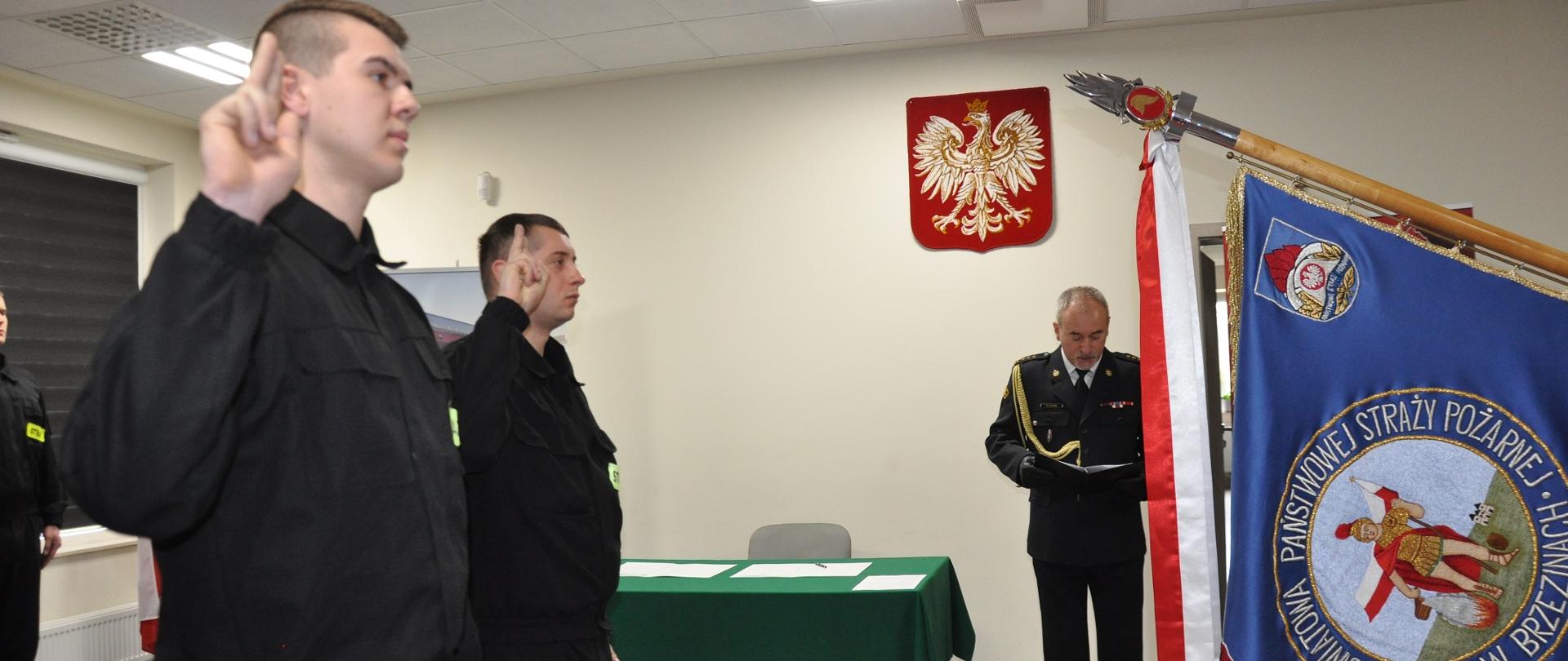 Dwóch nowo przyjętych strażaków składa ślubowanie strażaka PSP w obecności Komendanta Powiatowego PSP w Brzezinach st. bryg. Dariusza Guzka w pomieszczeniach komendy powiatowej.