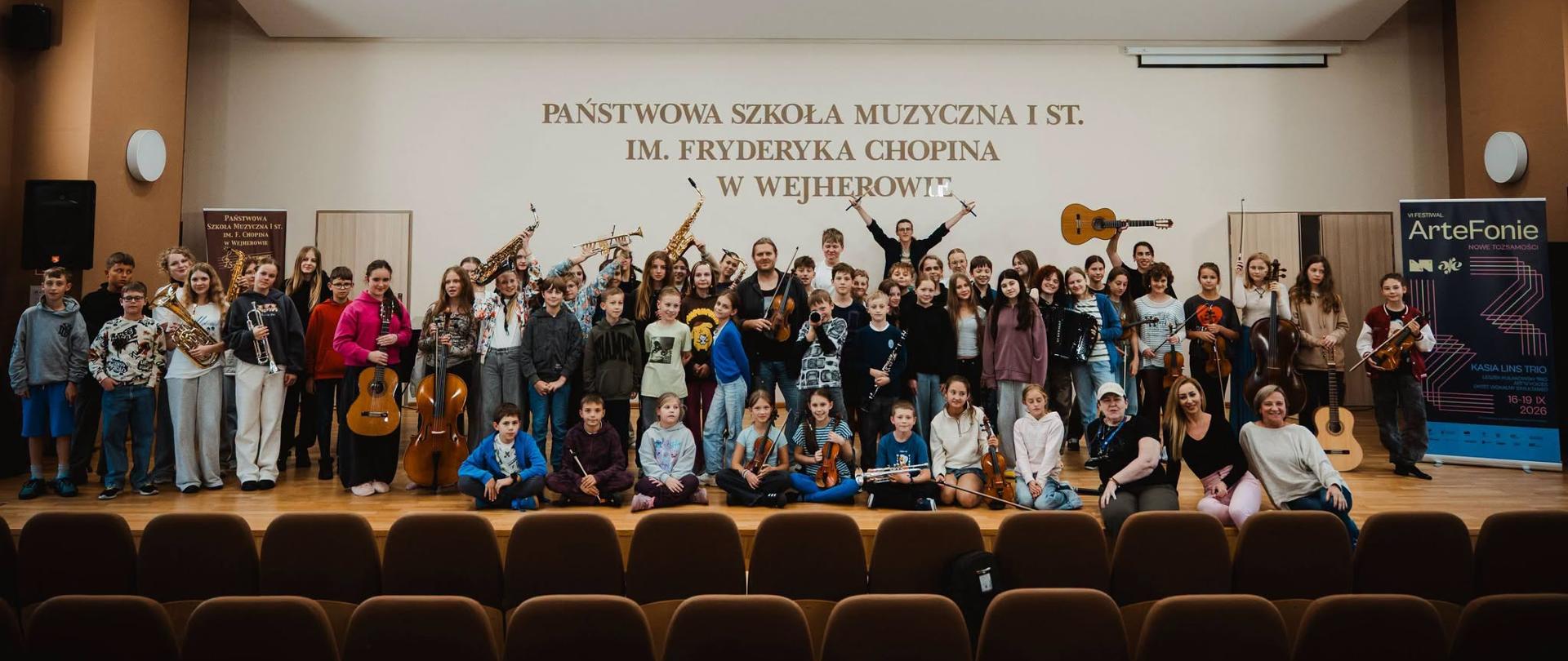 Wszyscy uczestnicy warsztatów pozują na estradzie trzymając swoje instrumenty