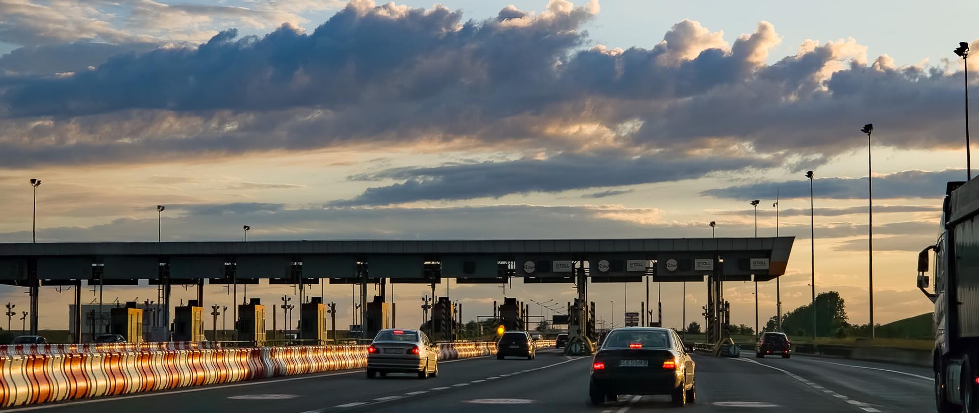 Ruch samochodowy na autostradzie A4 przed bramkami nieczynnego punktu poboru opłat Żernica koło Gliwic o zachodzie słońca, pod rozległym, chmurzystym niebem.