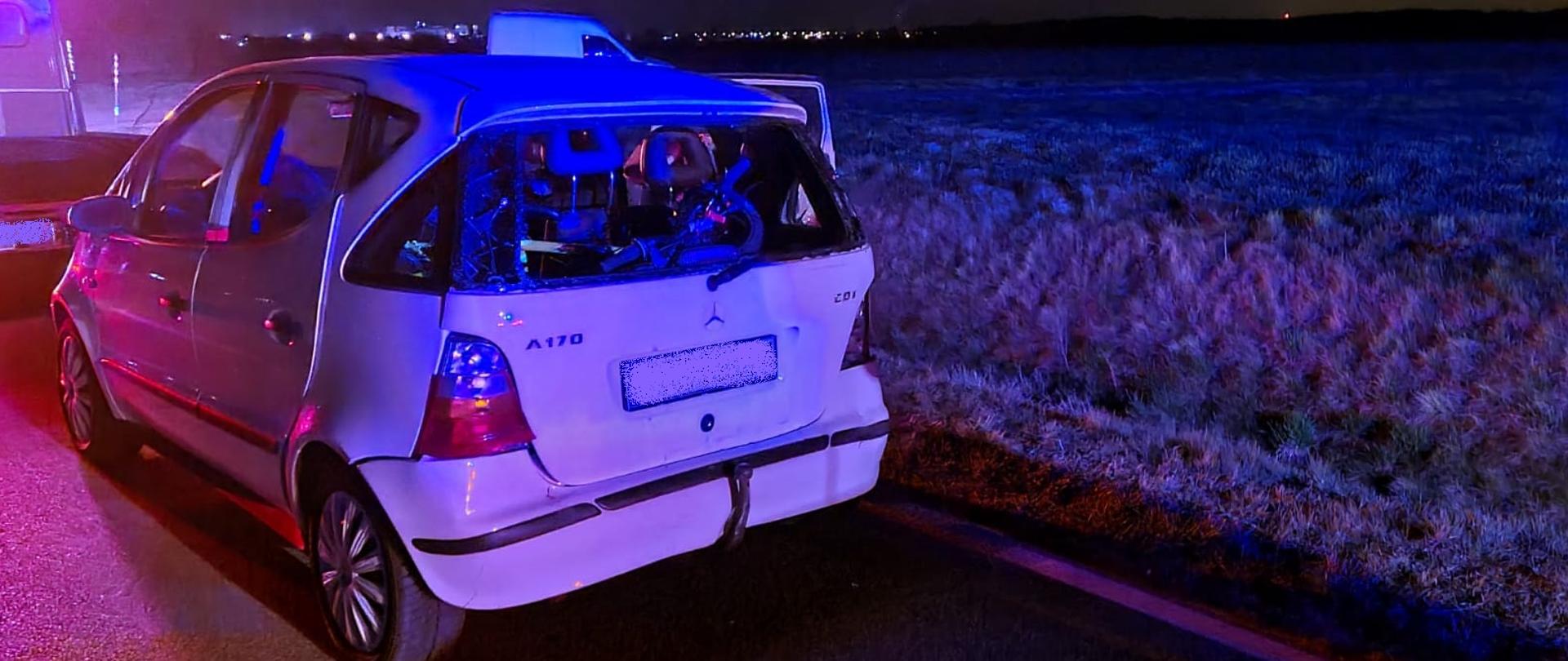 Widać biały samochód osobowy z uszkodzonym tyłem, jest ciemno