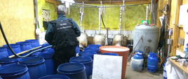 Funkcjonariusz Służby Celno-Skarbowej wśród beczek wewnątrz fabryki nielegalnego alkoholu.