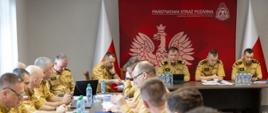 Opolski Komendant Wojewódzki PSP nadbryg. Paweł Kielar opowiada o ustawie oraz etapach jej wdrażania. Pozostali na sali funkcjonariusze to zastępcy opolskiego komendanta wojewódzkiego PSP, komendanci powiatowi i miejski (wraz z zastępcami) Państwowej Straży Pożarnej oraz naczelnicy wydziałów KW PSP w Opolu. Wszyscy strażacy w umundurowaniu służbowym. Narada w sali Komendy Wojewódzkiej PSP w Opolu.