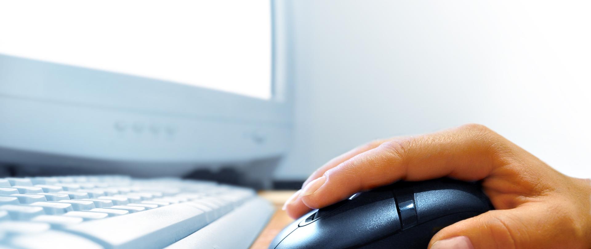 Na zdjęciu widać komputer, klawiaturę i myszkę obsługującą komputer.