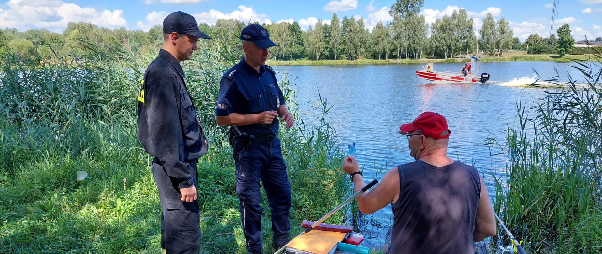 Zdjęcie przedstawia funkcjonariuszy patrolujących akweny wodne. Funkcjonariusze przypominają osobom wypoczywającym nad wodą o zasadach bezpiecznego wypoczynku.