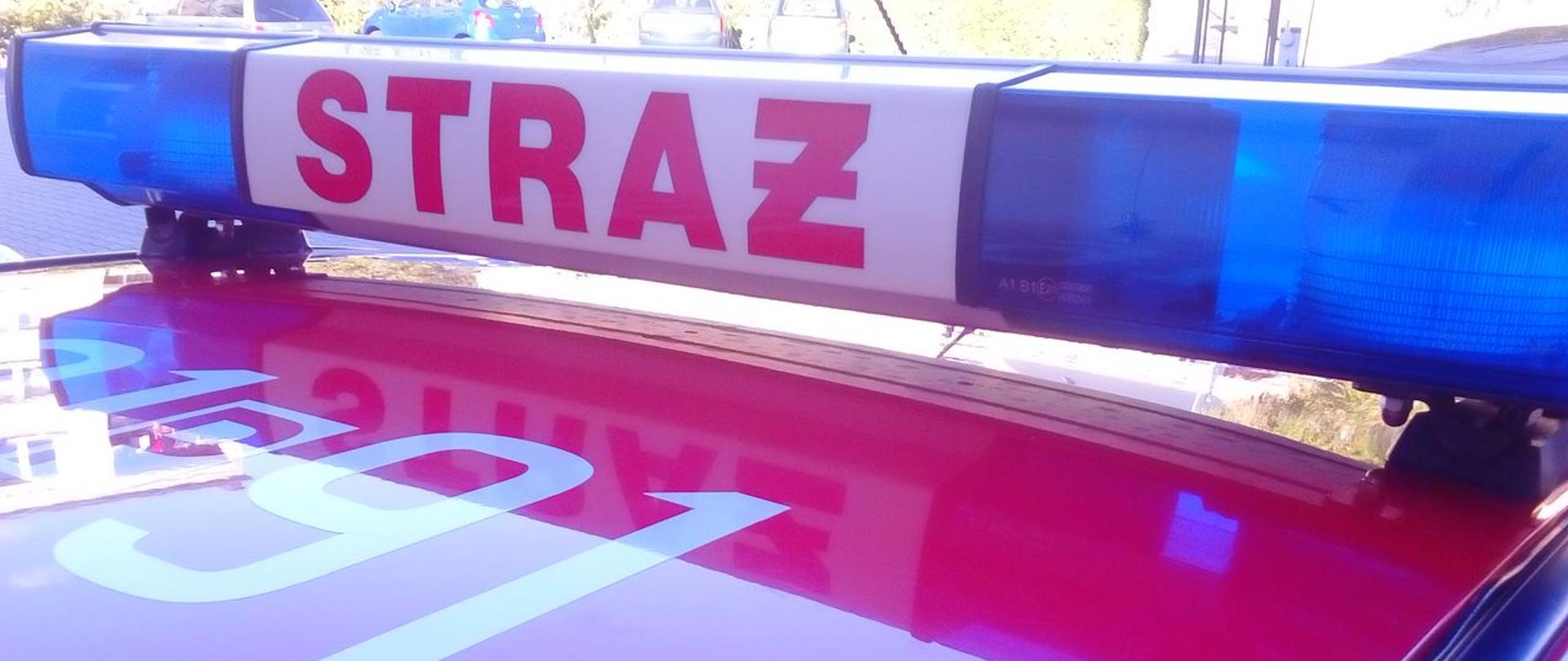 Zdjęcie przedstawia samochód strażacki.
W tle plac Komendy. 