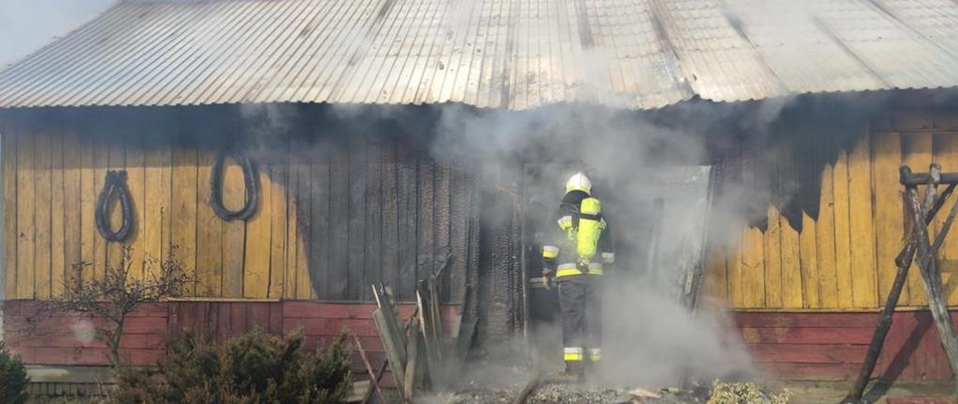 Dwóch strażaków ubranych w sprzęt ochrony układu oddechowego wchodzi do pomieszczenia budynku mieszkalnego z linia gaśniczą