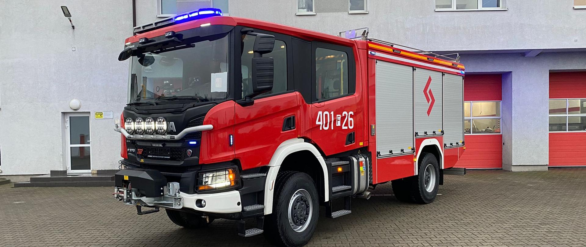 Fotografia przedstawia samochód pożarniczy - ciężki pojazd gaśniczy na tle budynku strażnicy JRG w Strzelcach Krajeńskich.