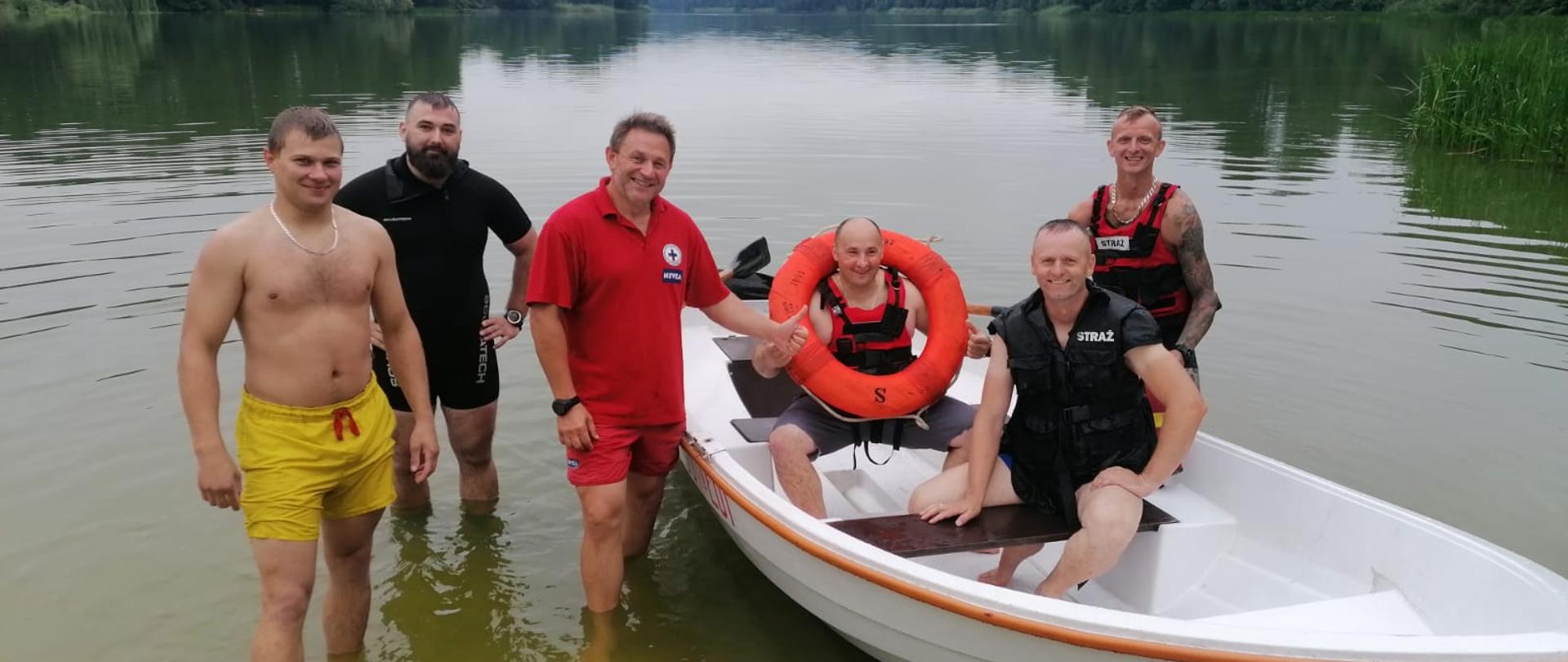 Zdjęcie przedstawia sześciu mężczyzn, dwóch z nich siedzi w łodzi reszta stoi w wodzie obok łodzi.