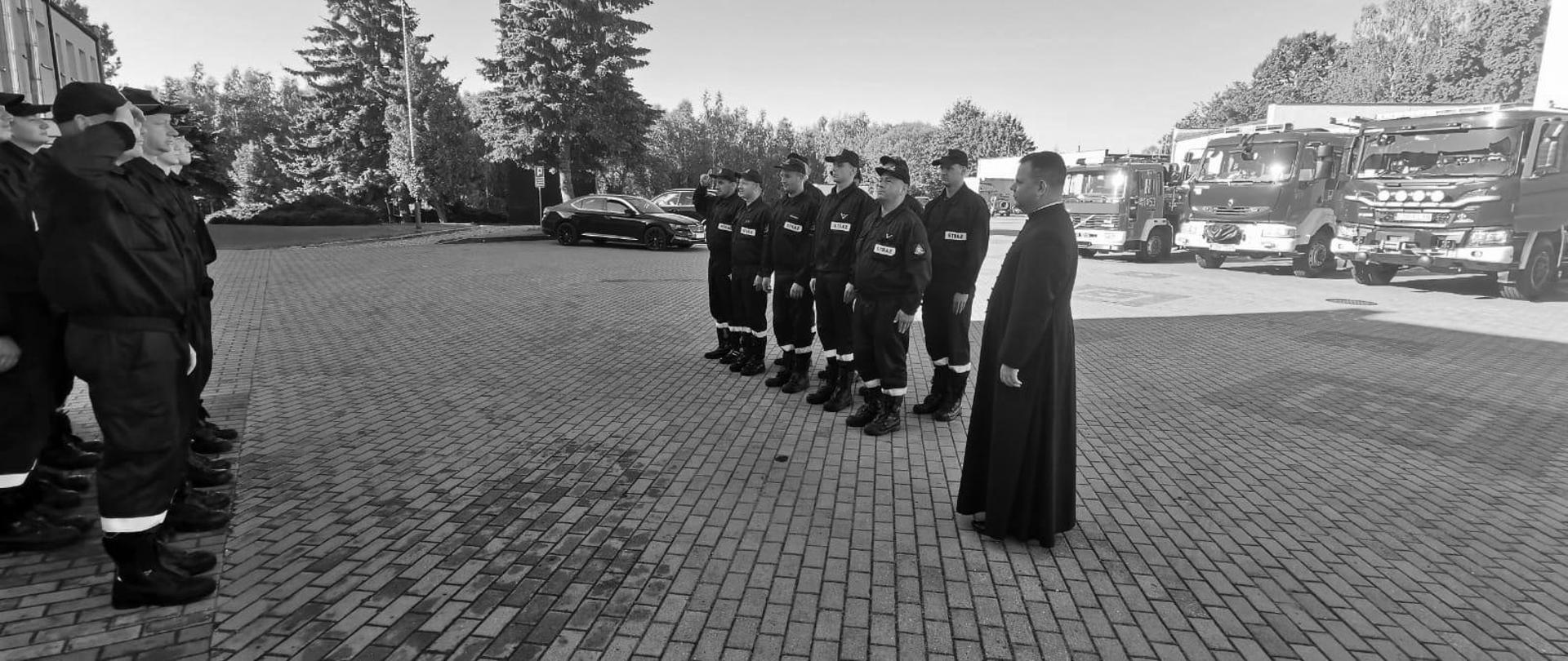 Zdjęcie przedstawia straszaków JRG Brodnica oddających hołd strażakowi Komendy Głównej PSP, który 6 sierpnia zginął w wypadku podczas służby. Na pierwszym planie ks. Mariusz Stasiak Kapelan Kujawsko-Pomorskich strażaków. W tle pojazdy ratowniczo - gaśnicze Komendy
