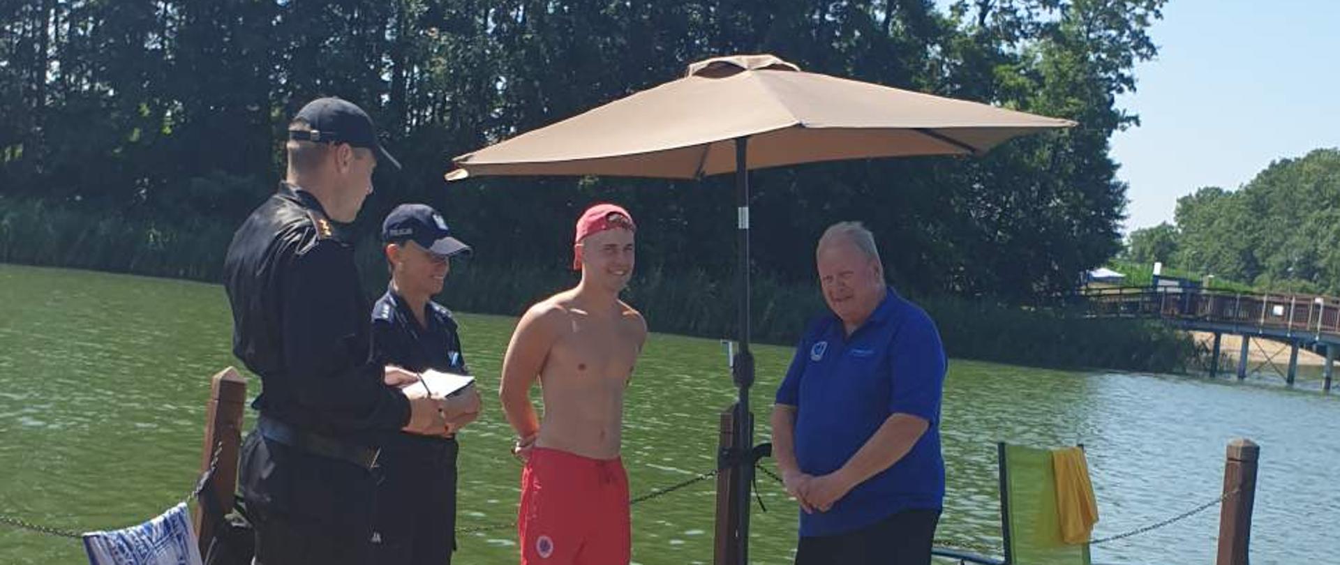 Zdjęcie przedstawia kąpielisko w czasie kontroli. Od lewej stoją dwaj strażacy, następnie ratownik WOPR, następnie V-ce Prezesem Wielkopolskiego Oddziału WOPR w Poznaniu. 