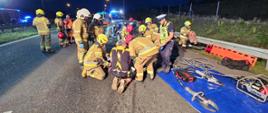 Na zdjęciu widać jak strażacy udzielają pomocy poszkodowanemu, którego ewakuowali z uszkodzonego pojazdu przy użyciu narzędzi hydraulicznych.