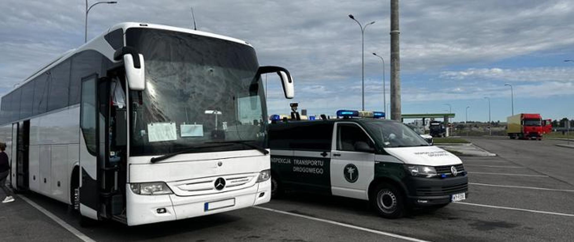 Autobus zatrzymany do kontroli na parkingu, obok którego stoi pojazd służbowy Inspekcji Transportu Drogowego