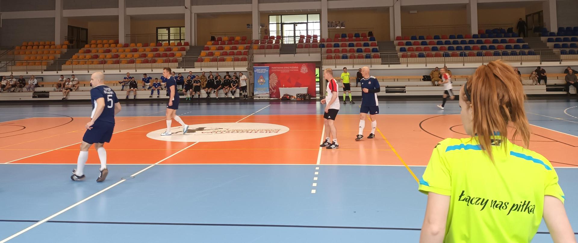 Zawodnicy podczas meczu, na pierwszym planie sędzia z napisem Łączy nas piłka
