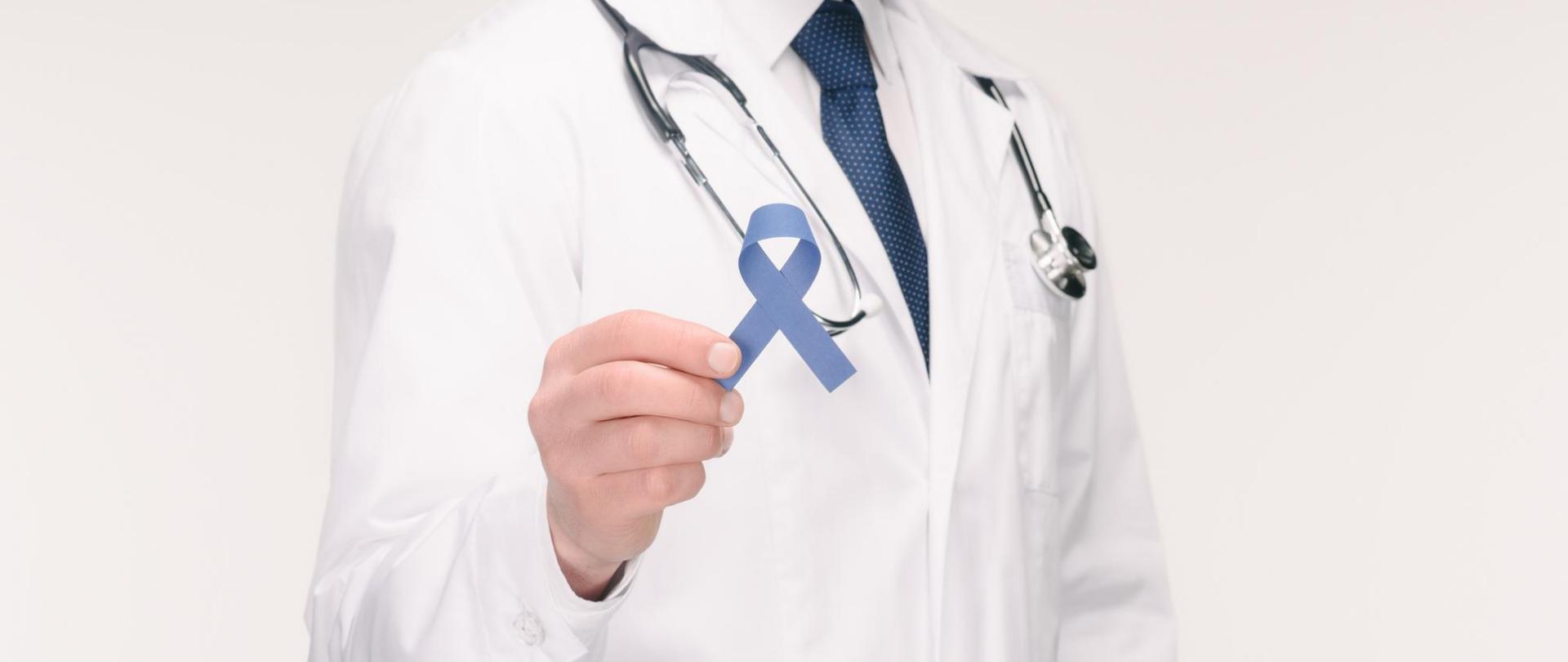 Na zdjęciu jest lekarz trzymający w dłoni ciemnoniebieską wstążkę.