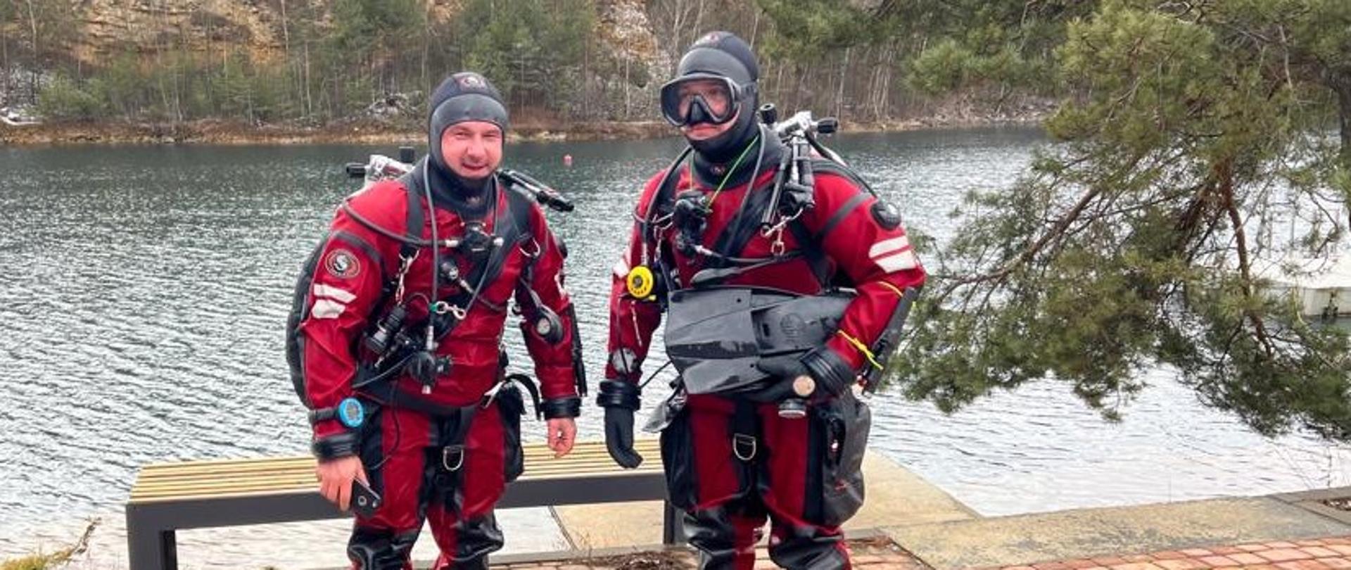 Dwóch nurków stojących na tle zbiornika wodnego ubranych w skafandry